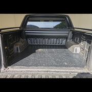 A black textured diamond-plate style truck bed liner installed inside the bed of a pickup truck, shown from the rear with the tailgate open.